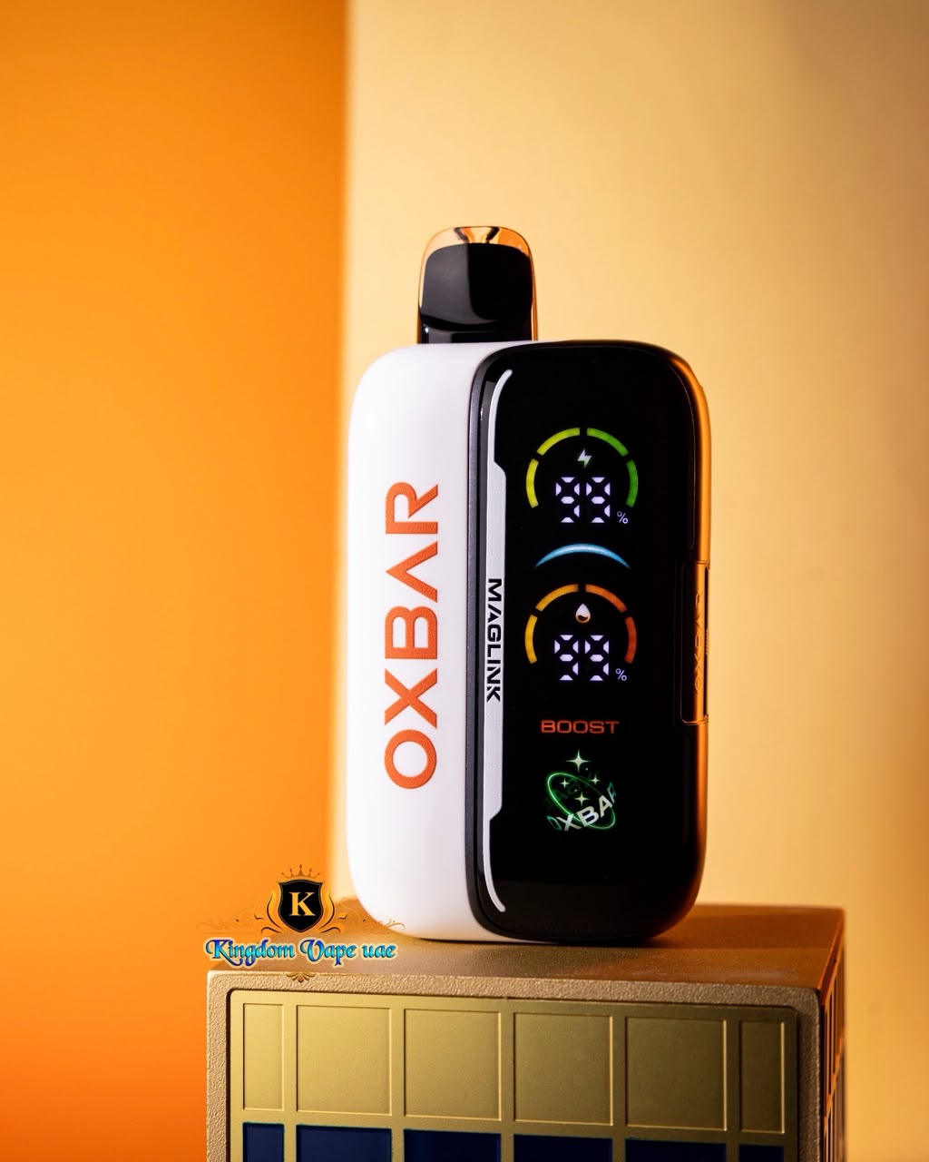An OXBAR vape device with a white and black body stands on a gold-colored display stand against a warm orange and yellow gradient background. The device features a digital screen on the front showing graphics and the text 'OXBAR' and 'MAGLINK BOOST'.